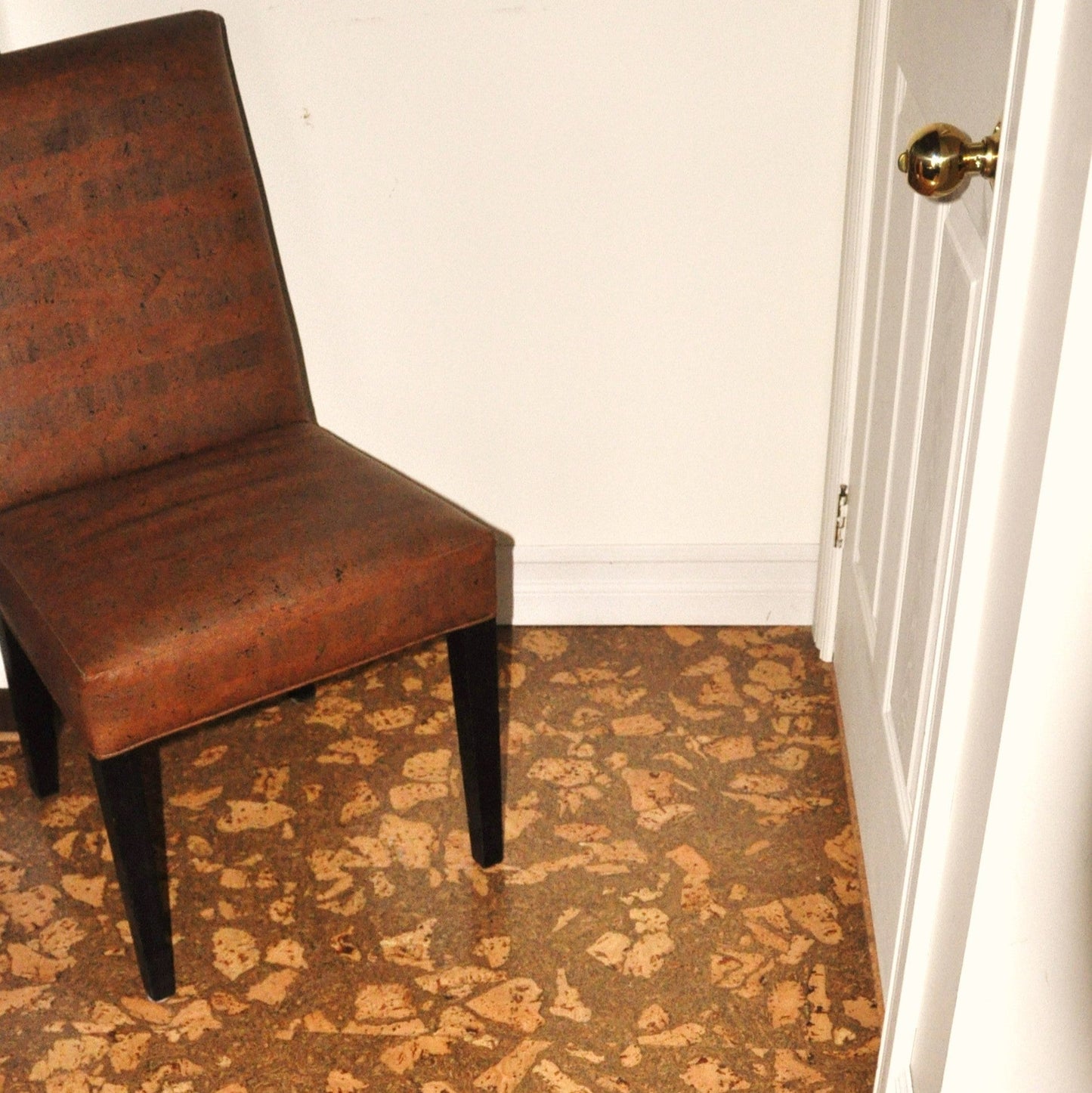 Brown chair on a patterned brown and beige corkstone cork flooring next to a white wall.