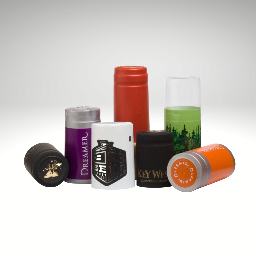 Collection of preformed custom shrink caps with various designs and colors on a white background. 