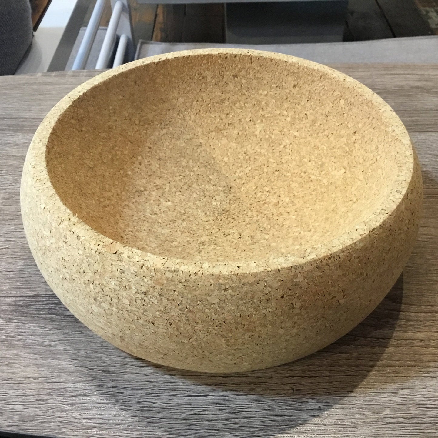A molded agglomerated cork fruit bowl sitting on a grey wood table. 